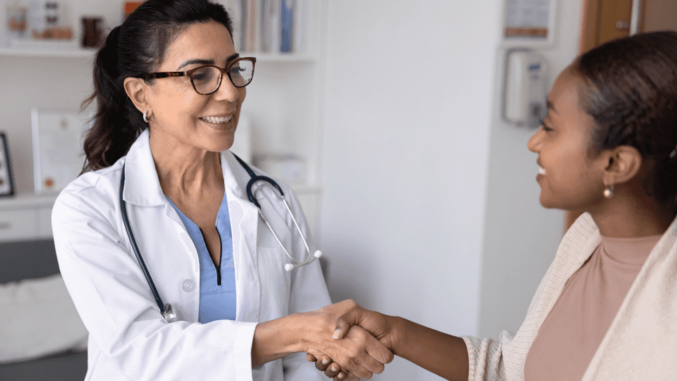 A healthcare provider shakes hands with a Black woman during a medical appointment
