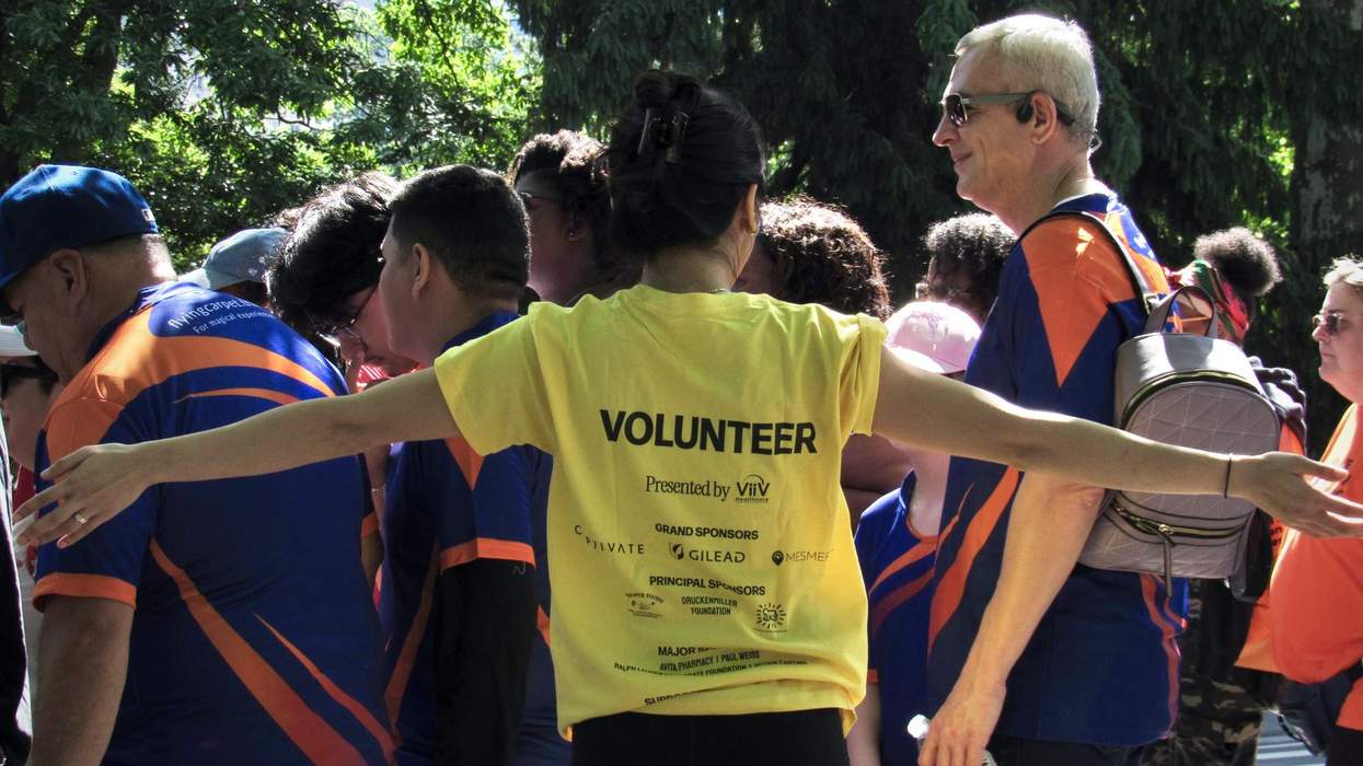 A person in a yellow "volunteer" shirt waves a crowd of walkers through a park.