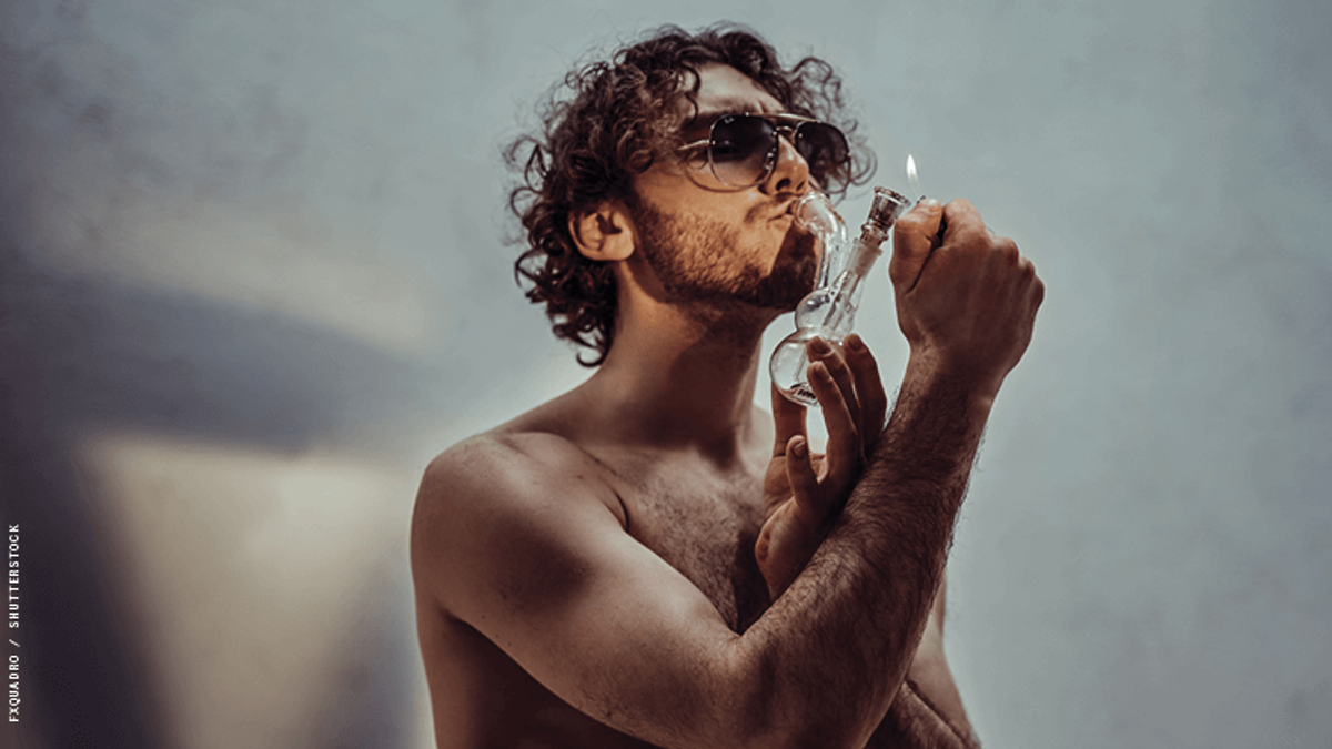 a shirtless man smoking weed through a bong