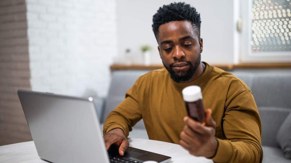 black man in front of a computer looks at a bottle of pills