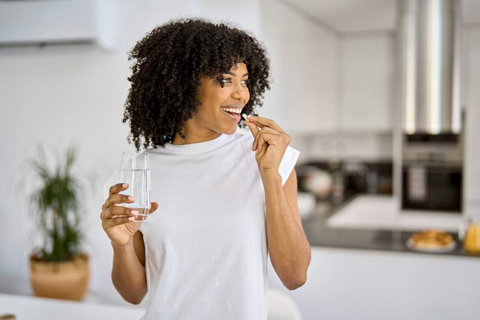 happy black woman taking a pill with water