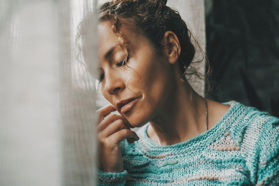 Woman leaning against a window with her eyes closed